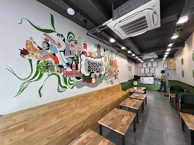 Indoor seating at Chai Kings Kelambakkam showing wooden bench seating below a colorful Chennai-themed wall mural.